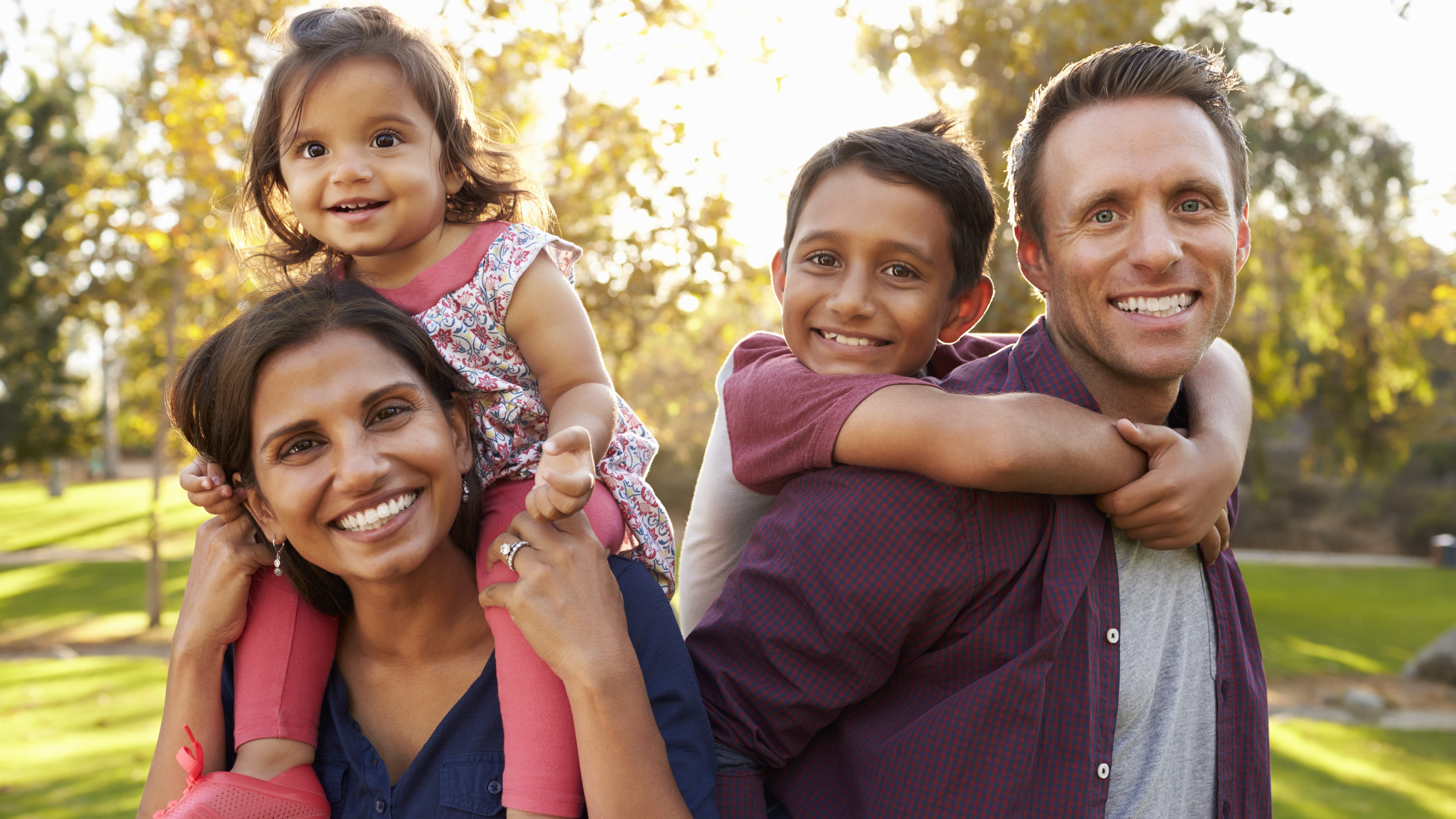 A woman with a female toddler on her shoulders and a man giving a boy a piggy-back ride.